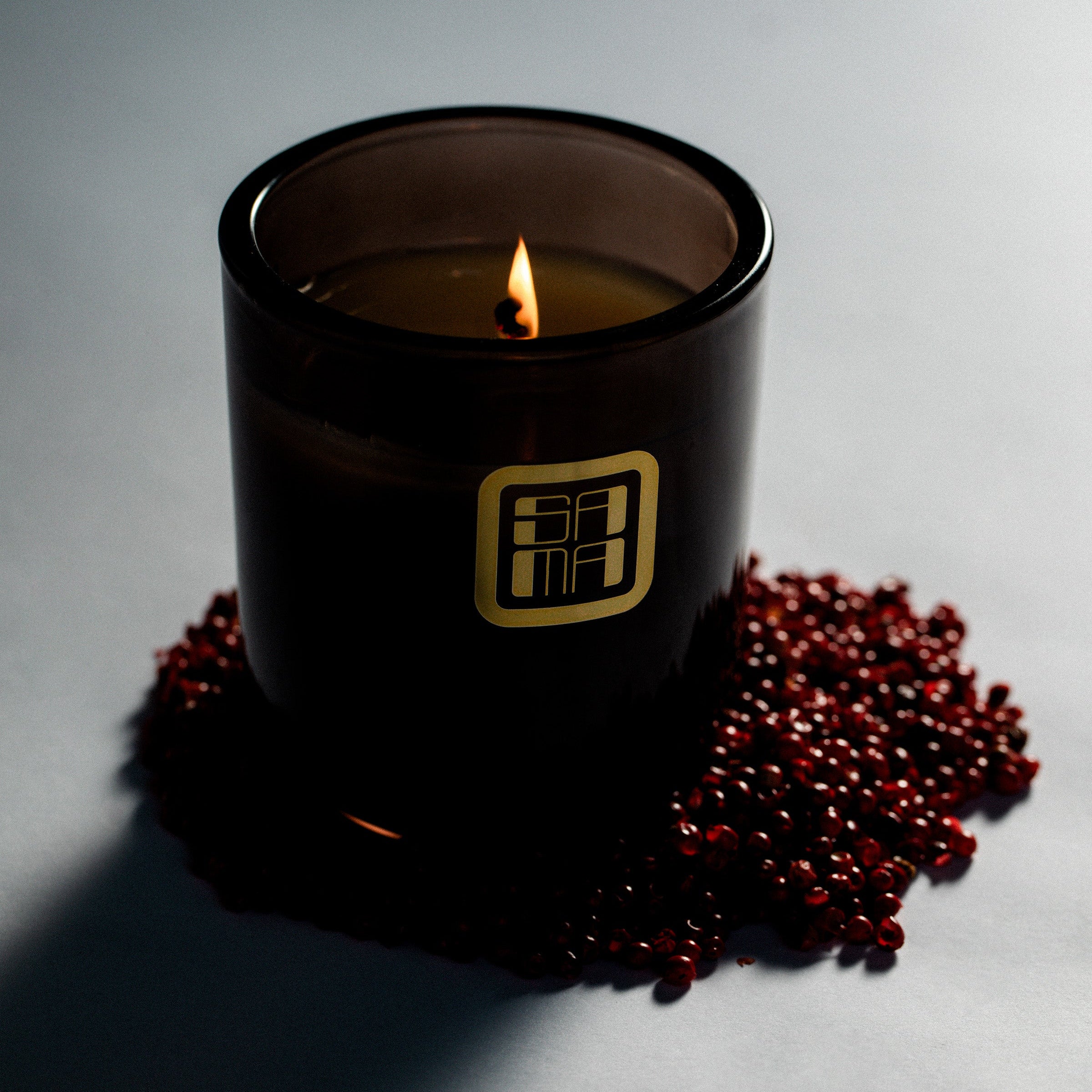 Black candle with a gold logo on a gray surface