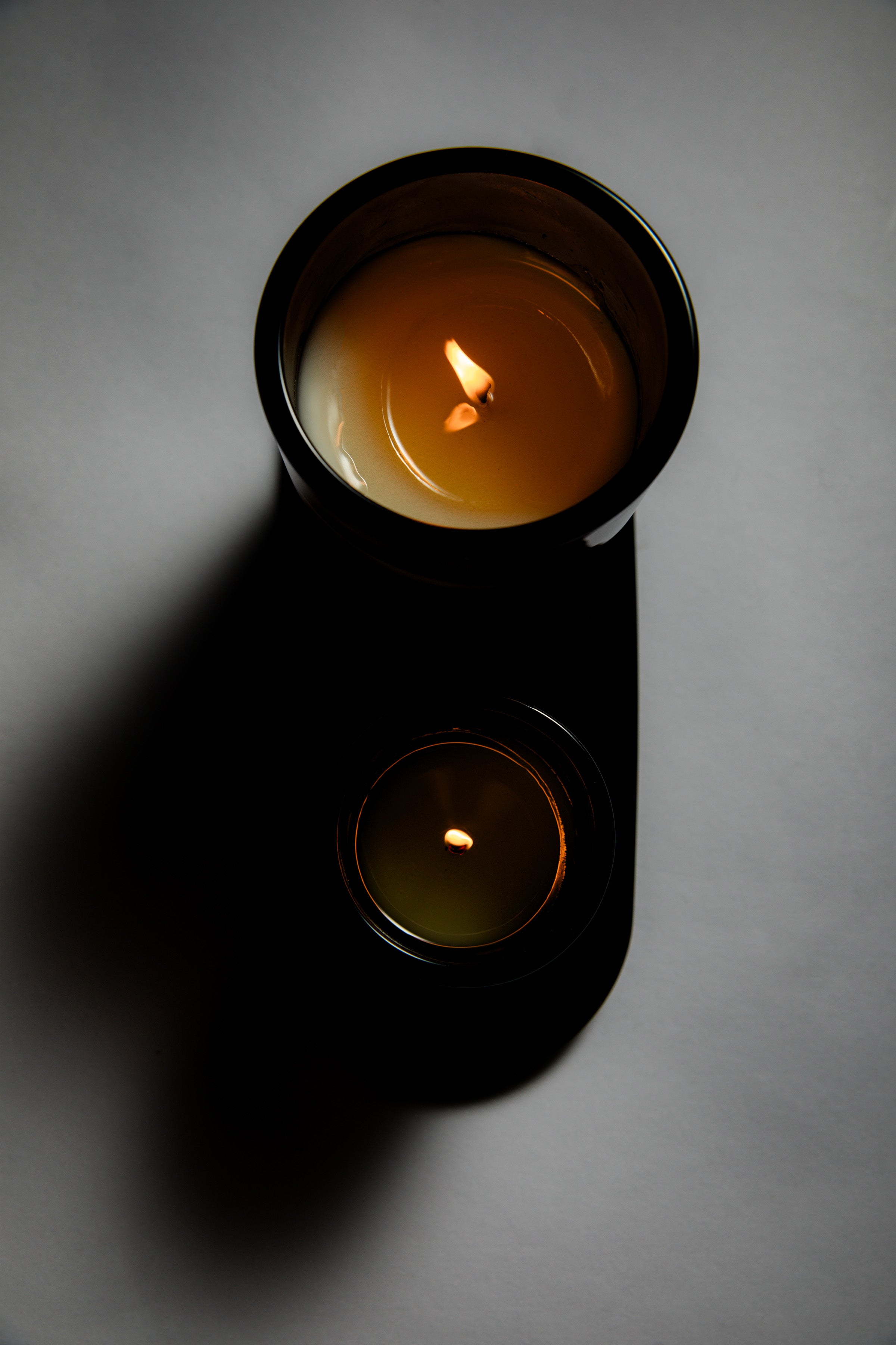 Two candles in black containers on a gray surface