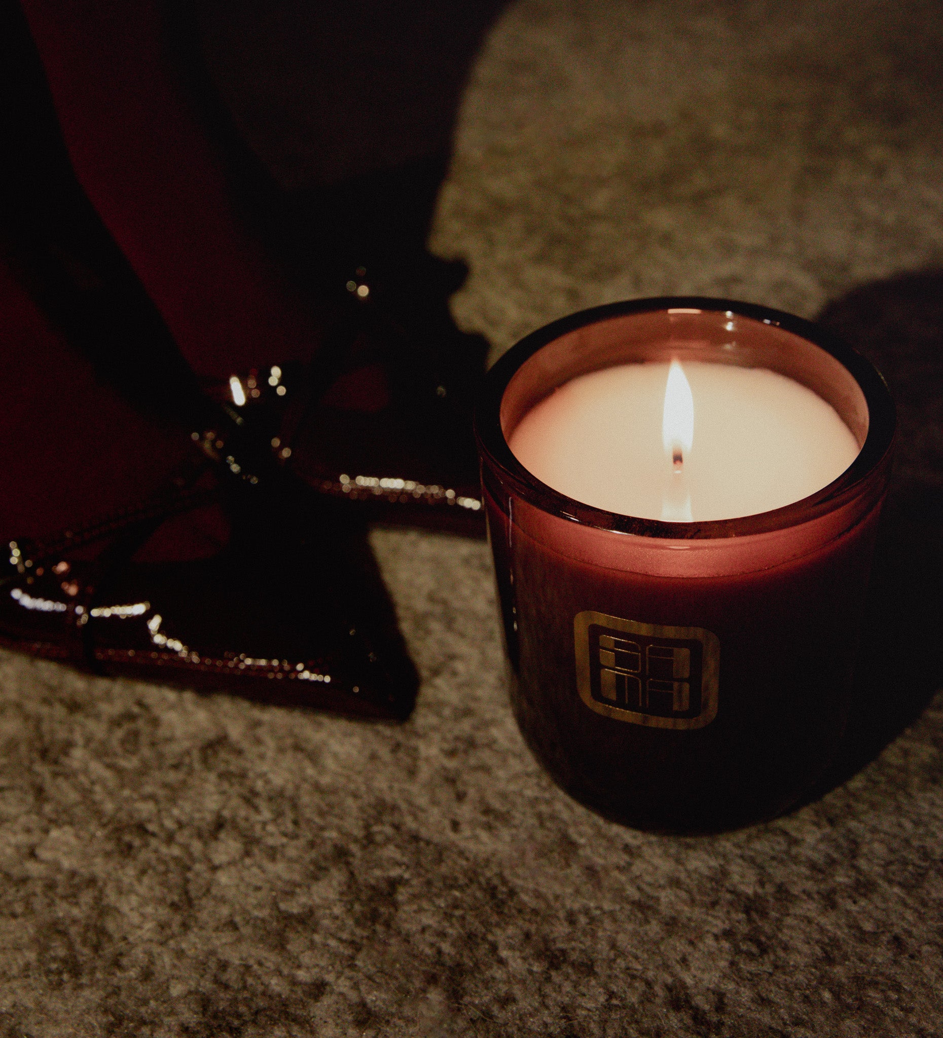 Candle in a brown holder with a logo on a textured surface