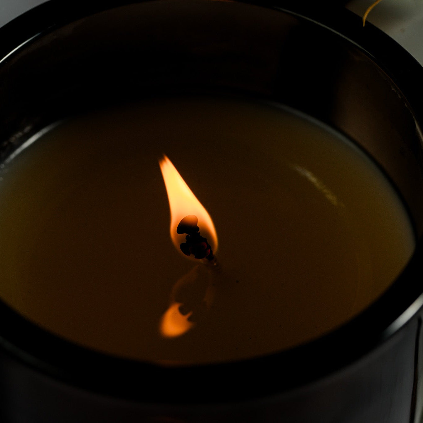Candle in a black container with a small flame on a dark background