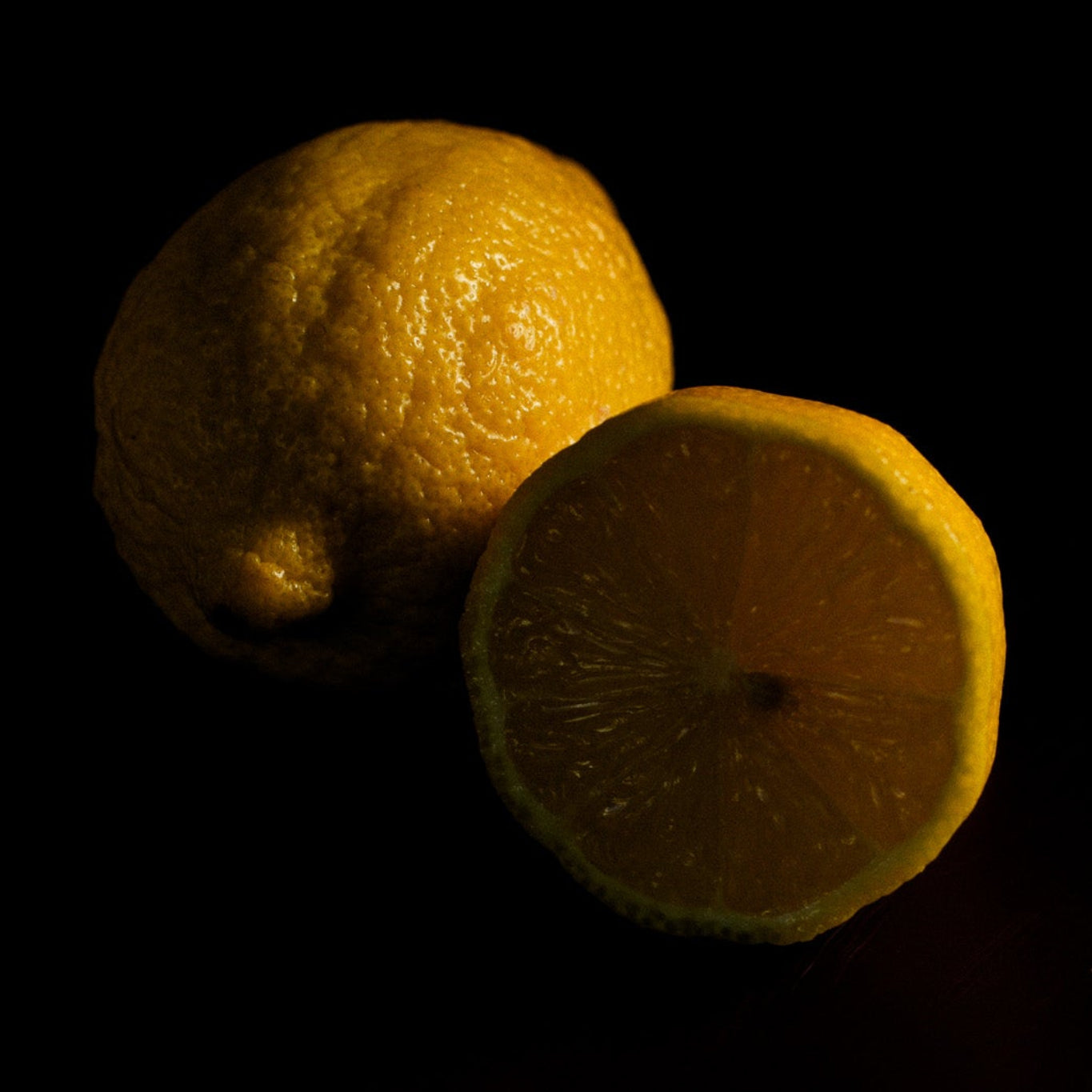 Two lemons, one whole and one sliced, on a black background
