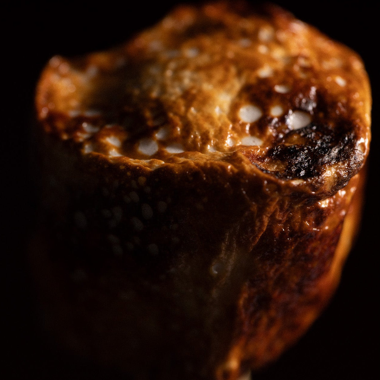 Close-up of a roasted marshmallow on a stick against a black background
