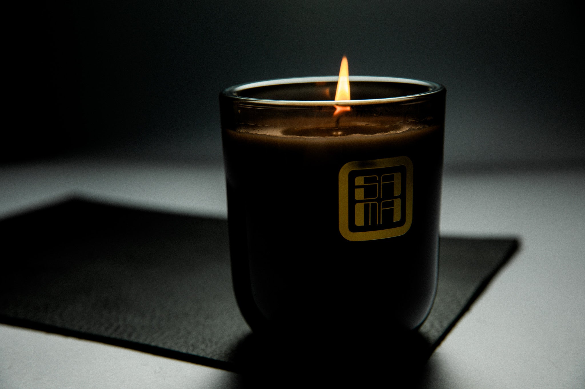 Candle in a black container with a logo on a dark surface