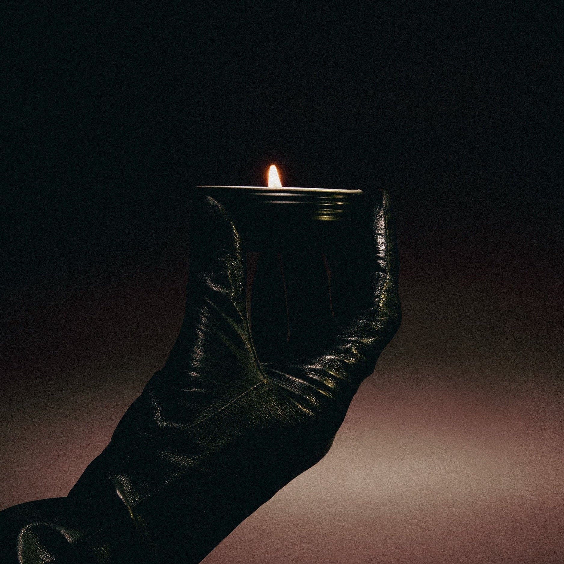 Dark leather boot holding a lit candle against a dark background