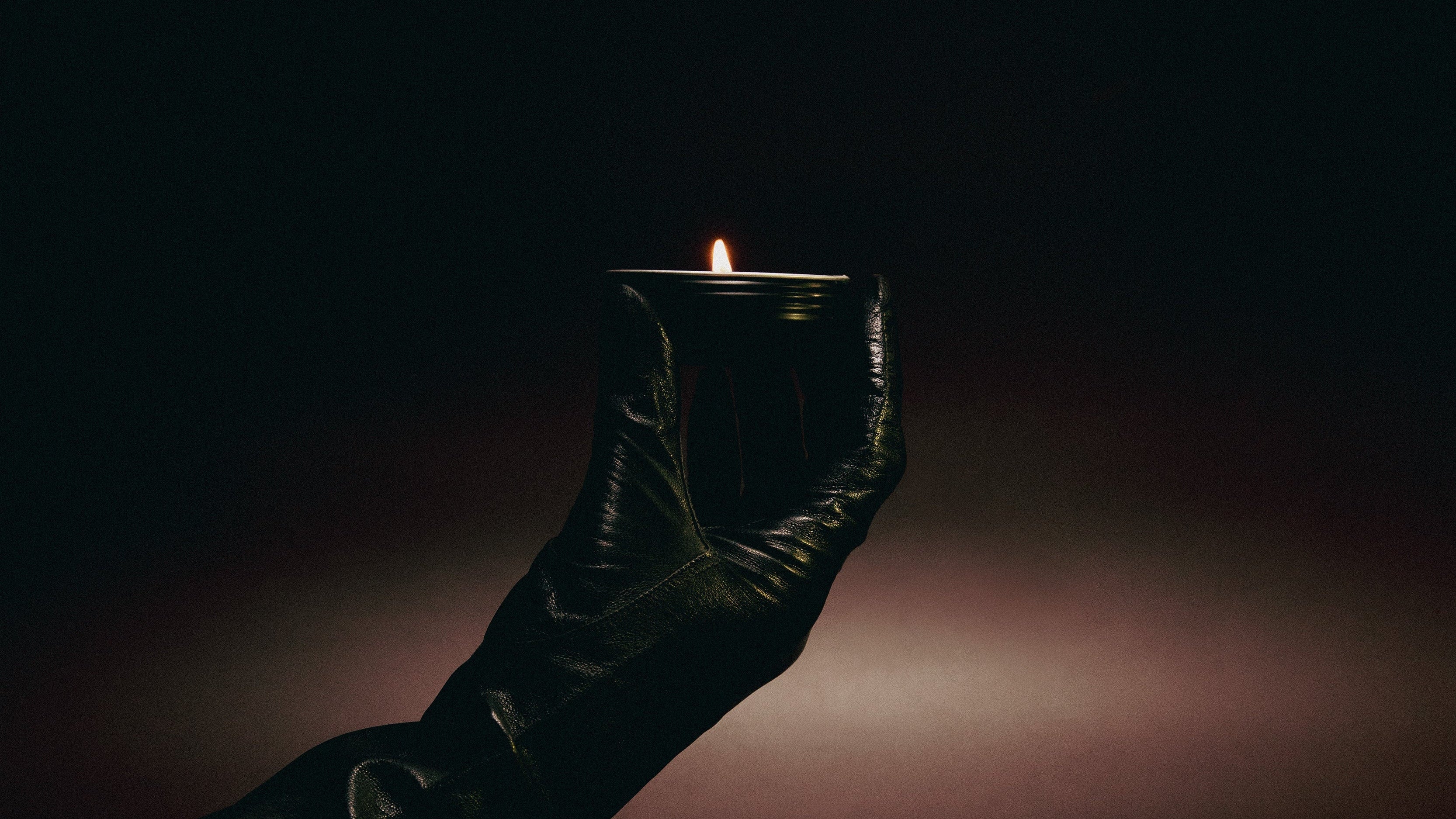 Dark leather boot holding a lit candle against a dark background