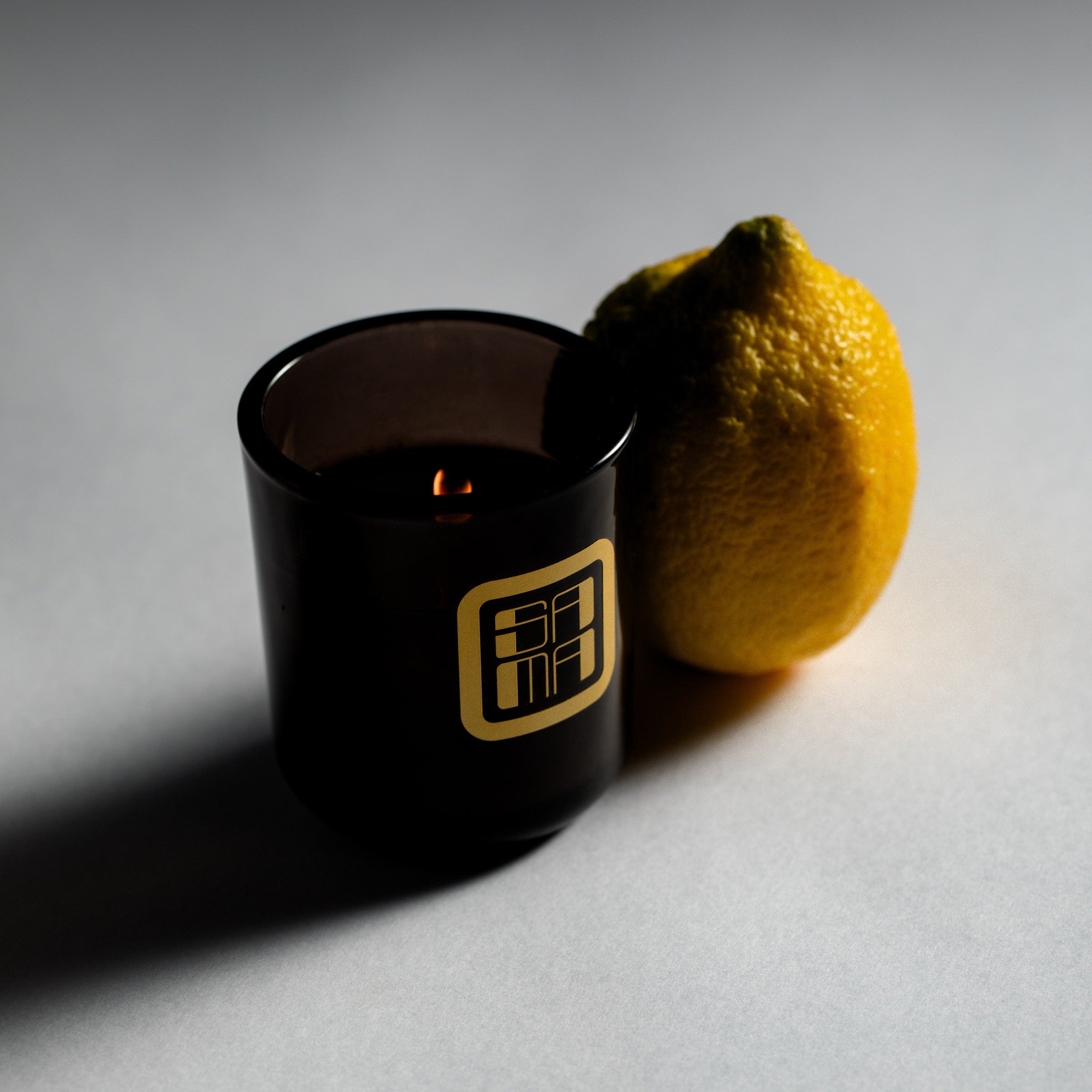 Black candle with a lemon next to it on a gray background